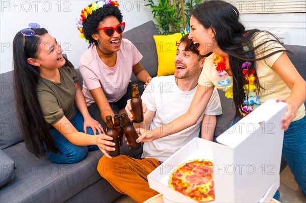 Multi-ethnic friends toasting with beer while eating pizza and celebrating birthday sitting on the sofa