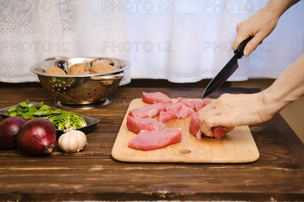 Female hands slicing raw pork fillet for ragout in the kitchen