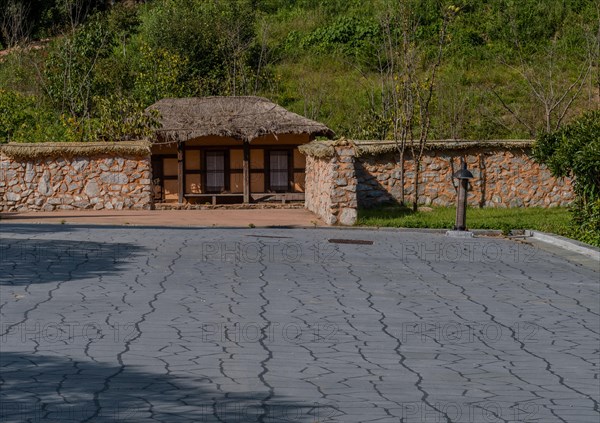 Old thatch roof building behind mud and stone wall at urban public park