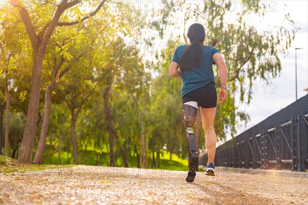 Rear view of a sportsperson with prosthetic leg running along a park