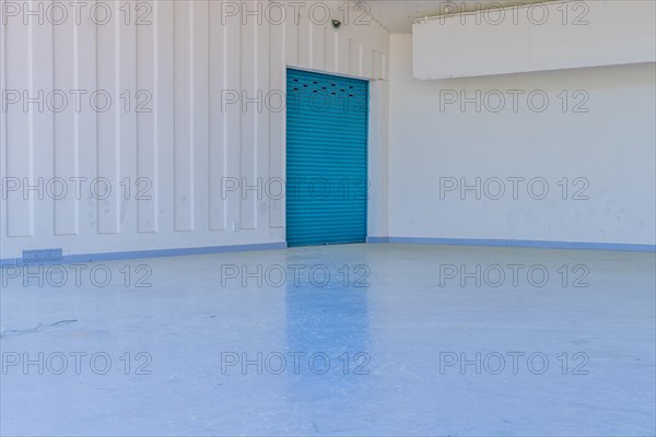Large blue metal door in white wall reflecting onto concrete floor of amphitheater in urban public park