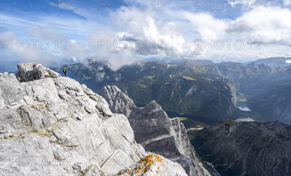 Mountaineer on the rocky summit of the Watzmann Mittelspitze, Watzmann crossing, view of mountain panorama with Steinernes Meer and Koenigssee, Berchtesgaden National Park, Berchtesgaden Alps, Bavaria, Germany, Europe