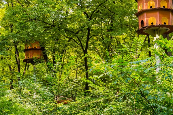Two large brown birdhouses on white poles in dense forest in public park