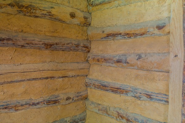 Interior corner of two walls of log cabin made of logs and held together with dried mud