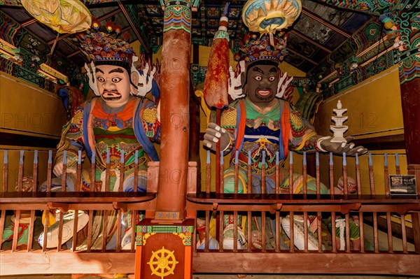 Wood carved statues of two Buddhist deities in covered pavilion at temple