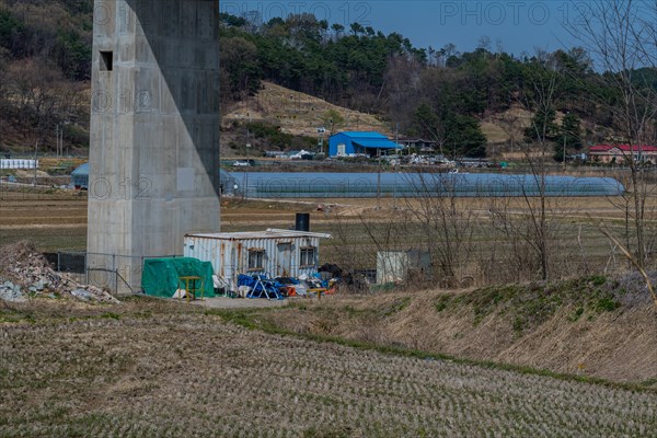 White metal storage building surrounded by debris beside concrete bridge support column