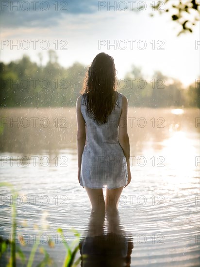 Suicidal thoughts, a young depressive woman with suicidal intent stands in the water by a lake in the rain, AI generated, AI generated