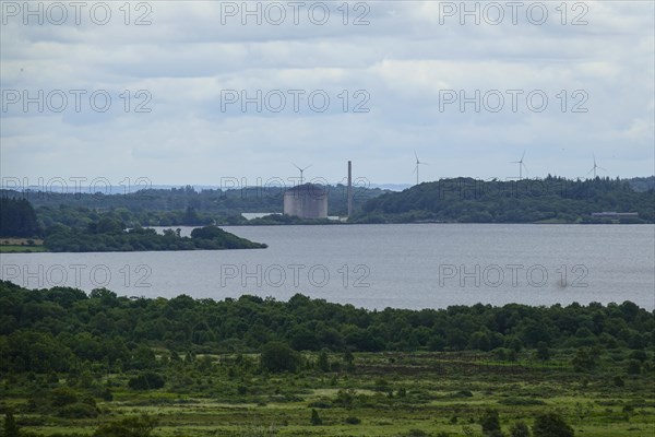 Former nuclear power plant Centrale nucleaire de Brennilis at the Reservoir de Saint-Michel, behind it wind turbines, wind farm, mountain range Monts d'Arree, department Finistere, region Brittany, France, Europe