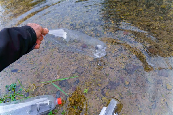 Man collecting plastic bottles on the shore of a river, environmental and ecological concept