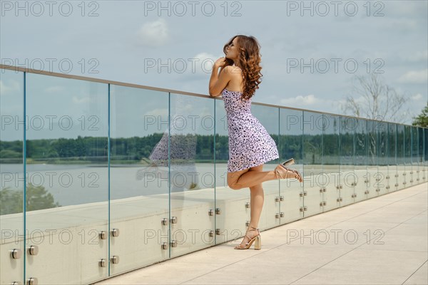 Slender woman in sundress with straps leans on glass railing of observation deck