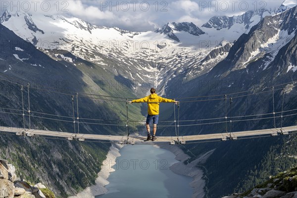 Mountaineers on a suspension bridge, picturesque mountain landscape near the Olpererhuette, view of turquoise-blue lake Schlegeisspeicher, glaciated rocky mountain peaks Hoher Weisszint and Hochfeiler with glacier Schlegeiskees, Berliner Hoehenweg, Zillertal Alps, Tyrol, Austria, Europe