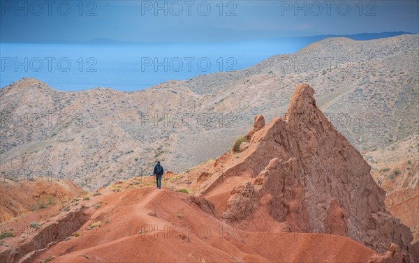 Hiker in front of eroded mountain landscape, sandstone cliffs, canyon with red and orange rock formations, Konorchek Canyon, Chuy, Kyrgyzstan, Asia
