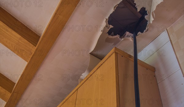 Large hole and torn wallpaper in ceiling above kitchen cabinets in abandoned house