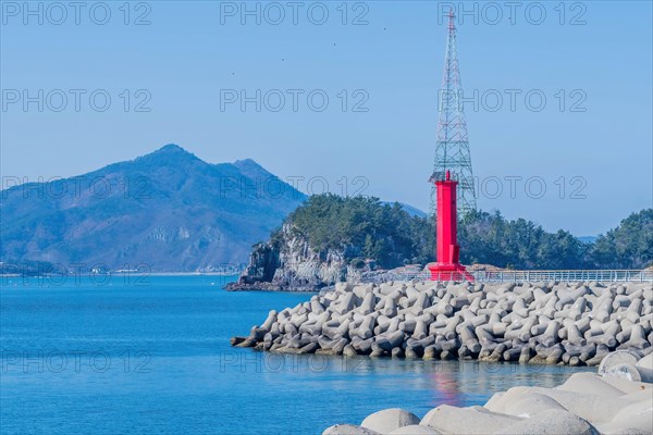 Red lighthouse on concrete pier in small coastal fishing port