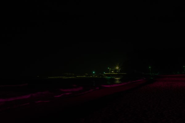 Night scene of deserted beach in darkness with waves coming into shore and street lights over road in background