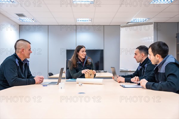 Manager leading a meeting with engineers in a factory room with table and board
