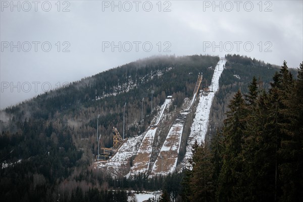 A ski jump tower stands on a snowy mountain slope with cloudy skies above, czech harrachov