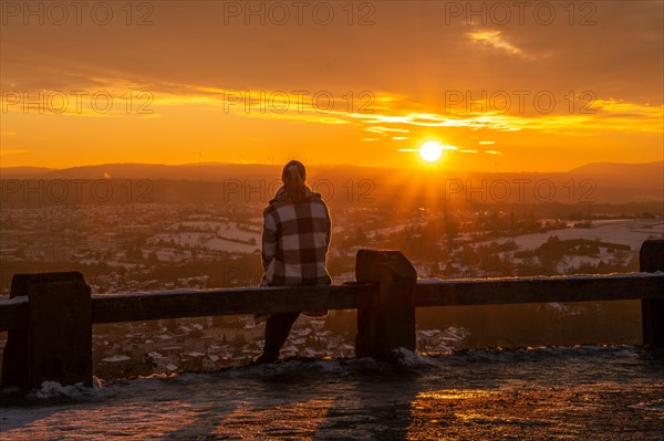 Person sitting on a wooden railing looking at the sunset over a wintry landscape, Wallberg, Pforzheim, Germany, Europe