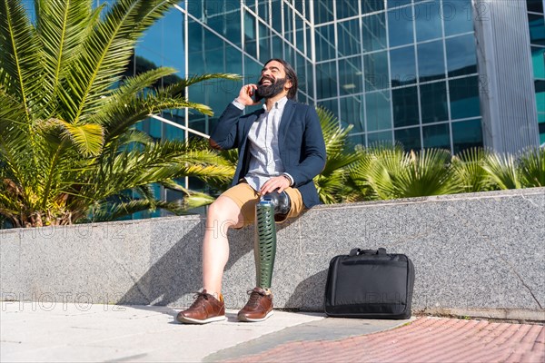 Happy businessman with prosthetic leg talking to the mobile sitting outside a financial building