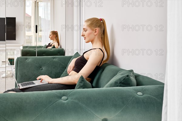 Active woman in sportswear sitting on sofa and establishing connection with trainer online