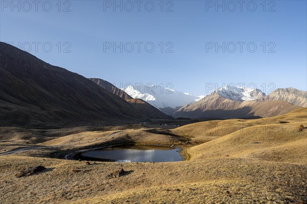 White glaciated and snow-covered mountain peak Pik Lenin at sunrise, mountain landscape with golden hills and small lakes, Trans Alay Mountains, Pamir Mountains, Osh Province, Kyrgyzstan, Asia