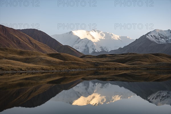 White glaciated and snowy mountain peak Pik Lenin at sunset, mountains reflected in a lake between golden hills, Trans Alay Mountains, Pamir Mountains, Osh Province, Kyrgyzstan, Asia