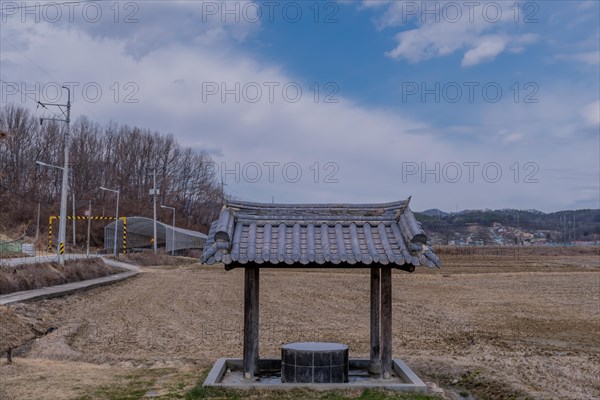 Covered water well under ceramic tiled roof full of water in a mountainside public park with plowed field in background