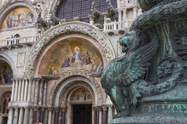 Old street ornament with winged lions and San Marco Basilica in the background, in St. Mark Square, famous tourist attraction in Venice, Italy. Selective focus