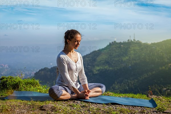 Sporty fit woman practices yoga asana Baddha Konasana, bound angle pose outdoors in Himalayas mountains in the morning. Himachal Pradesh, India, Asia