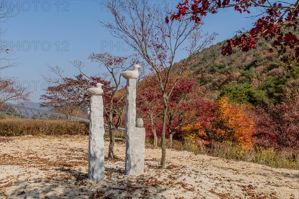 Stone carved ducks on vertical plinths in wilderness park with trees in fall colors