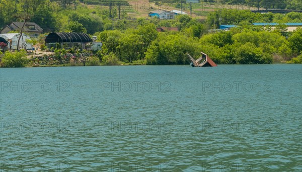 Abandoned floating fishing house partially submerged in water near far shore lake