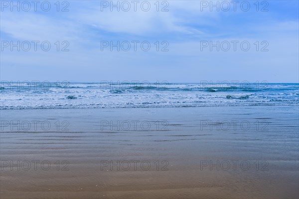 Sandy beach and rough ocean waves and white caps under a blue sky with low wispy cirrus clouds