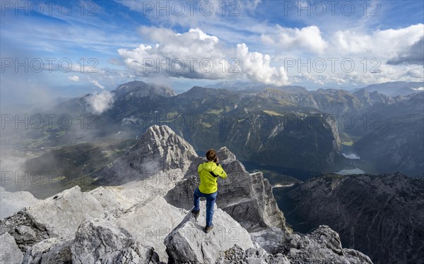 Mountaineer on the rocky summit of the Watzmann Mittelspitze, Watzmann crossing, view of mountain panorama with Steinernes Meer and Koenigssee, Kleiner Watzmann and Watzmann children, Berchtesgaden National Park, Berchtesgaden Alps, Bavaria, Germany, Europe