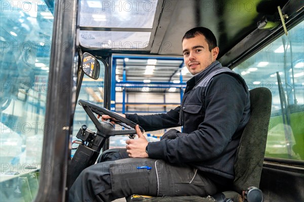 Male manual worker driving a forklift in a modern cnc logistic factory