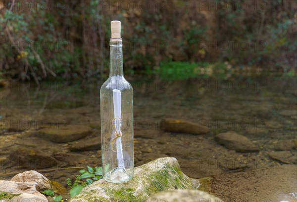 Glass bottle with a message inside on a rock on the shore of a lake