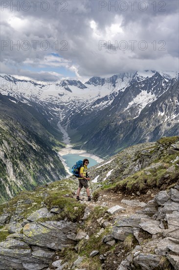 Mountaineer on hiking trail, view of Schlegeisspeicher, glaciated rocky mountain peaks Hoher Weisszint and Hochfeiler with glacier Schlegeiskees, Berliner Hoehenweg, Zillertal Alps, Tyrol, Austria, Europe