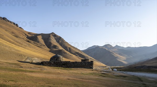 Historic caravanserai Tash Rabat from the 15th century, in the evening light with golden hills and yurts, Naryn region, Kyrgyzstan, Asia