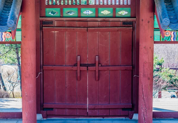 Red wooded gate with tiled roof and colorful, oriental design at a local woodland park in South Korea