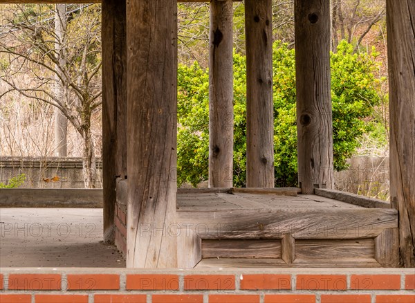 Inside view of old oriental style covered pavilion surrounded by a concrete wall in an overgrown woodland area in South Korea