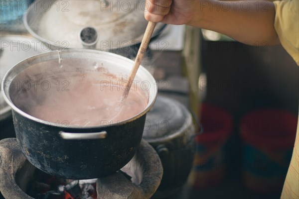 Close-up of a hand stirring a pot of sikwate or Filipino hot chocolate drink in a traditional kitchen showing the candid authentic daily life at home in rural Philippines