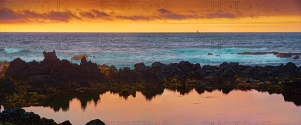 Panorama of the coastline at sunset with reflections on the water surface and a sailing boat in the background, Madalena, Pico, Azores, Portugal, Europe