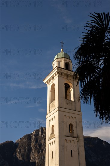 Church Bell Tower of San Zenone Against Blue Sky and Mountain Peak San Salvatore and Palm Leaf in Campione d'Italia, Lombardy, Italy, Europe