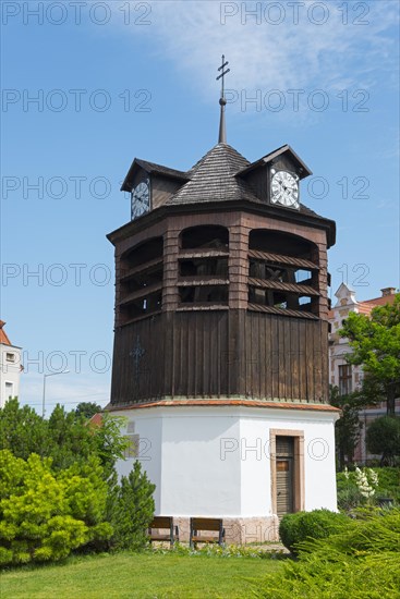 A wooden clock tower stands under a blue sky surrounded by trees and grass, Clock Tower, Oratorony, Tata, Totis, Lake Oereg, Komarom-Esztergom, Central Transdanubia, Hungary, Europe