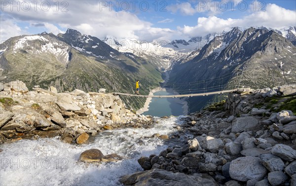 Mountaineers on a suspension bridge over a mountain stream Alelebach, picturesque mountain landscape near the Olpererhuette, view of turquoise-blue lake Schlegeisspeicher, glaciated rocky mountain peaks Grosser Moeseler, Hoher Weisszint and Hochfeilermit glacier Schlegeiskees, Berliner Hoehenweg, Zillertal Alps, Tyrol, Austria, Europe