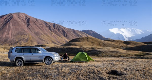 An off-road vehicle stands next to a pitched tent in a mountain landscape with snow-capped peaks in the background, Lenin Peak, Kyrgyzstan, Asia