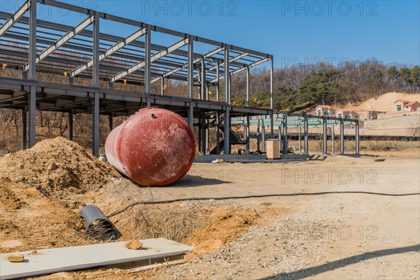 Chungju, South Korea, March 22, 2020: For editorial use only. Large round storage tank on ground in front of unfinished metal frame building at rural construction site, Asia