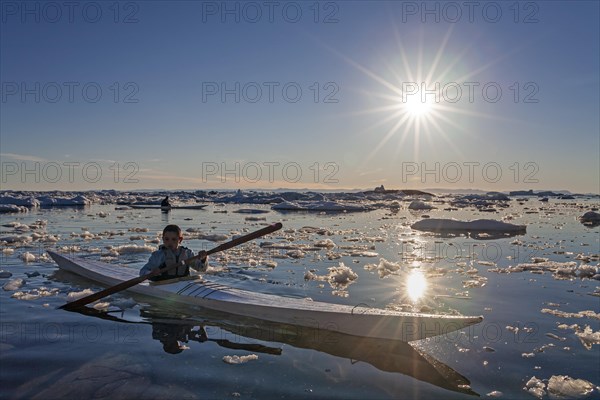 Child paddling in sea kayak through ice floes in the sea, kayak, backlight, sunbeams, summer, Ilulissat, Disko Bay, Greenland, North America