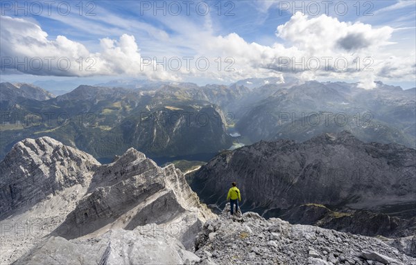 Mountaineer on the rocky summit of the Watzmann Mittelspitze, Watzmann crossing, view of mountain panorama with Steinernes Meer and Koenigssee, Berchtesgaden National Park, Berchtesgaden Alps, Bavaria, Germany, Europe