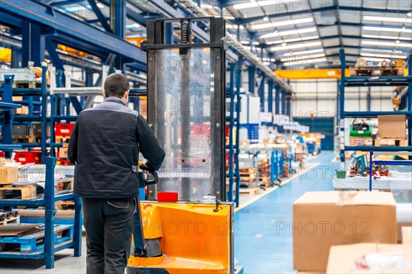 Warehouse worker walking among shelves with handcart in a logistic factory