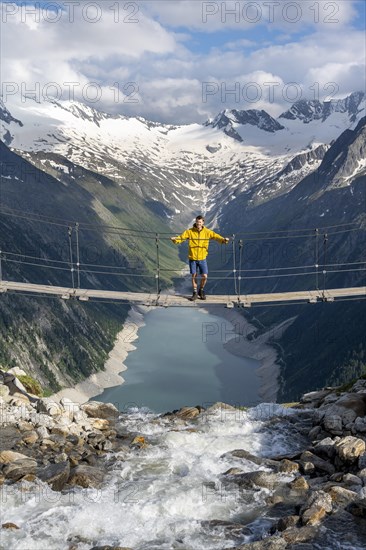 Mountaineers on a suspension bridge over a mountain stream Alelebach, picturesque mountain landscape near the Olpererhuette, view of turquoise-blue lake Schlegeisspeicher, glaciated rocky mountain peaks Hoher Weisszint and Hochfeiler with glacier Schlegeiskees, Berliner Hoehenweg, Zillertal Alps, Tyrol, Austria, Europe